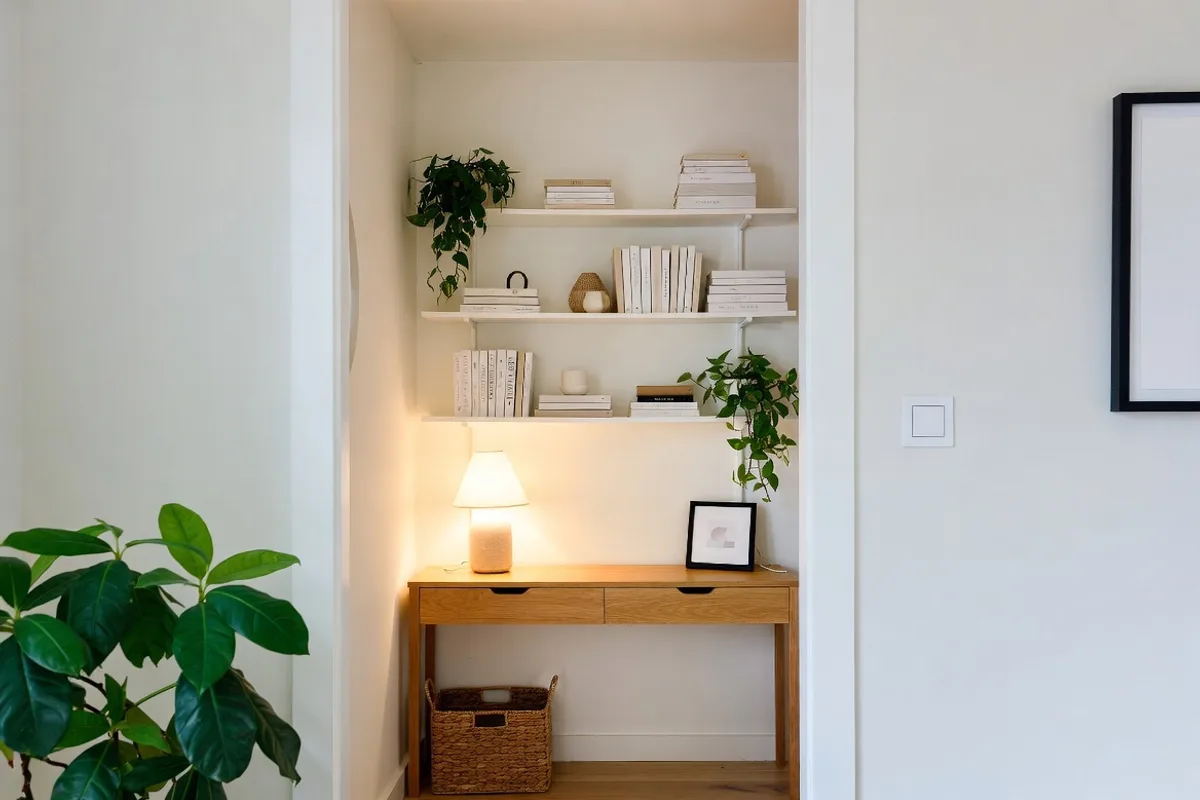 Vertical floating shelves styled with plants and books above a slim oak console table in a small living room corner