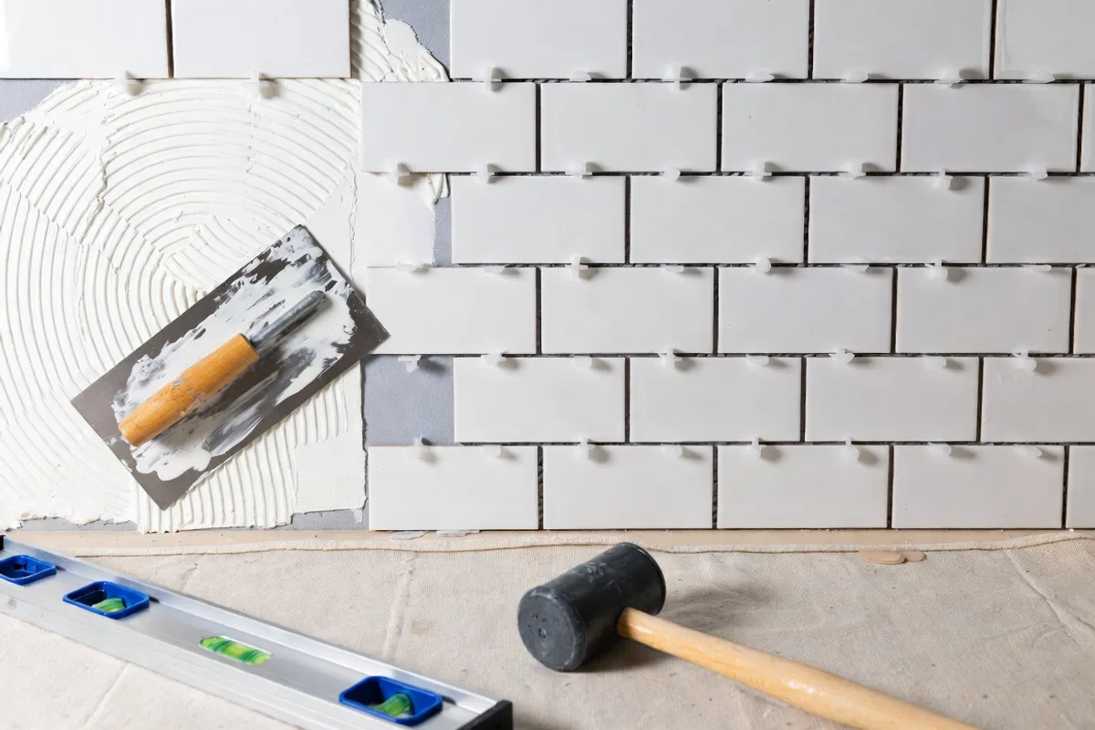 Close-up of subway tile installation in progress on kitchen wall showing tiles, spacers, notched trowel, and thinset adhesive
