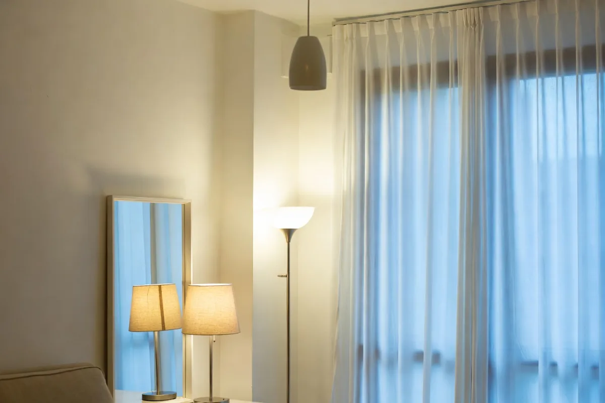 Small apartment living room with layered lighting using floor lamp, table lamp, and mirror to reflect natural light