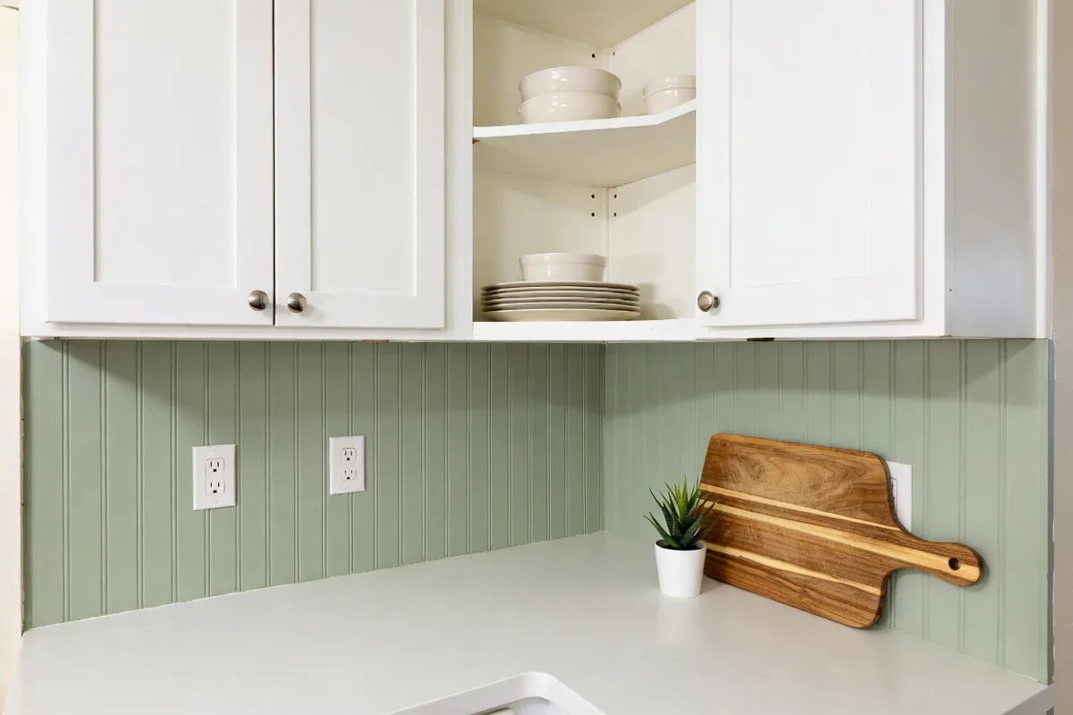 Sage green painted beadboard kitchen backsplash with white cabinets and open shelving