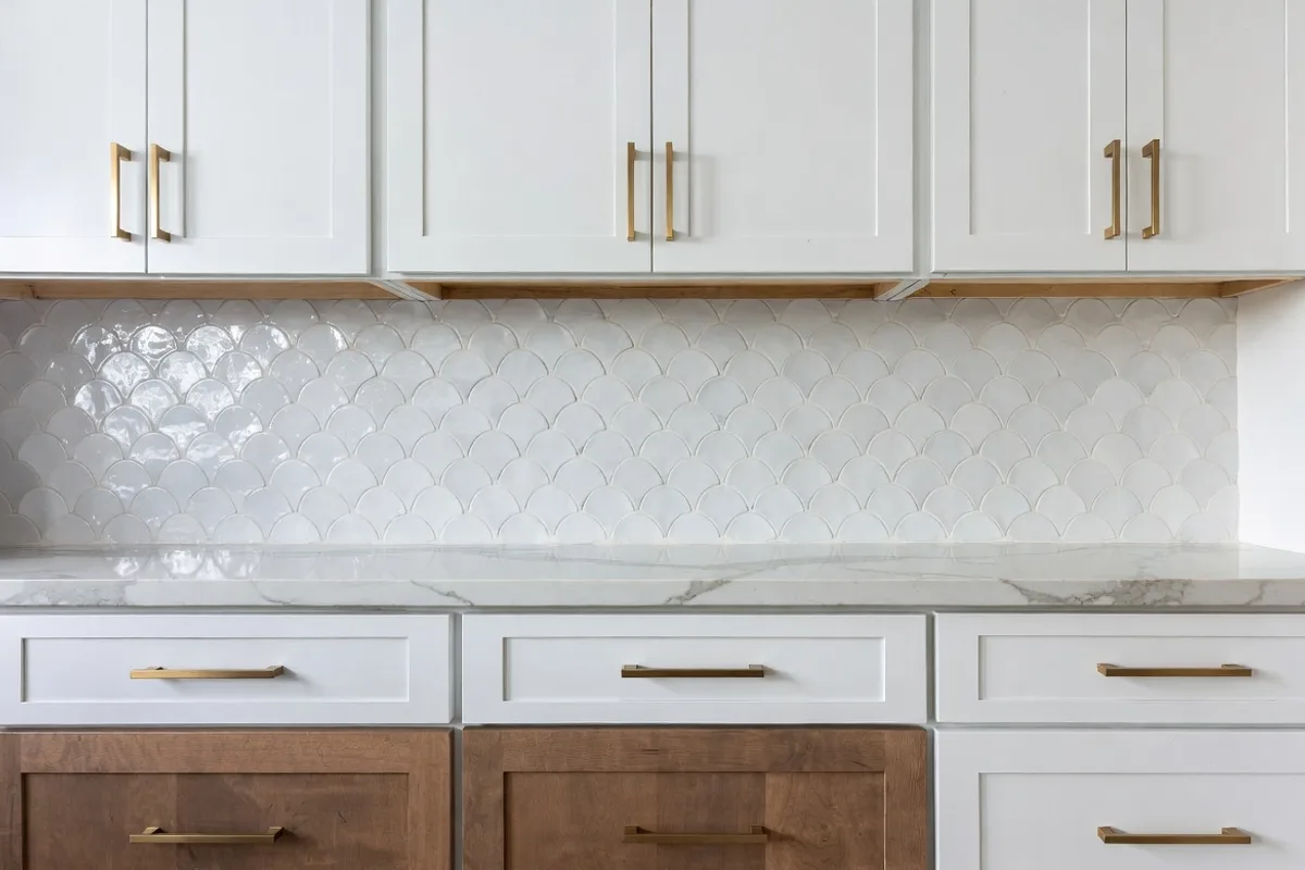 White scallop fish scale tile kitchen backsplash with warm wood cabinets and gold hardware